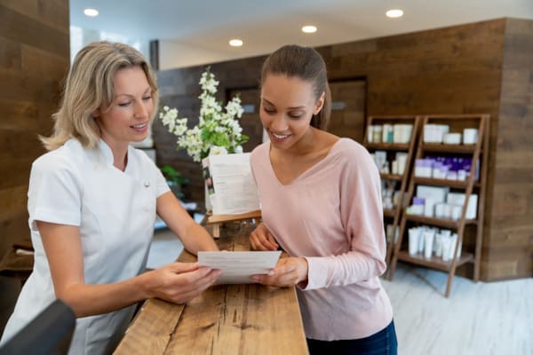A massage therapist at the front desk of a clinic speaking to a customer